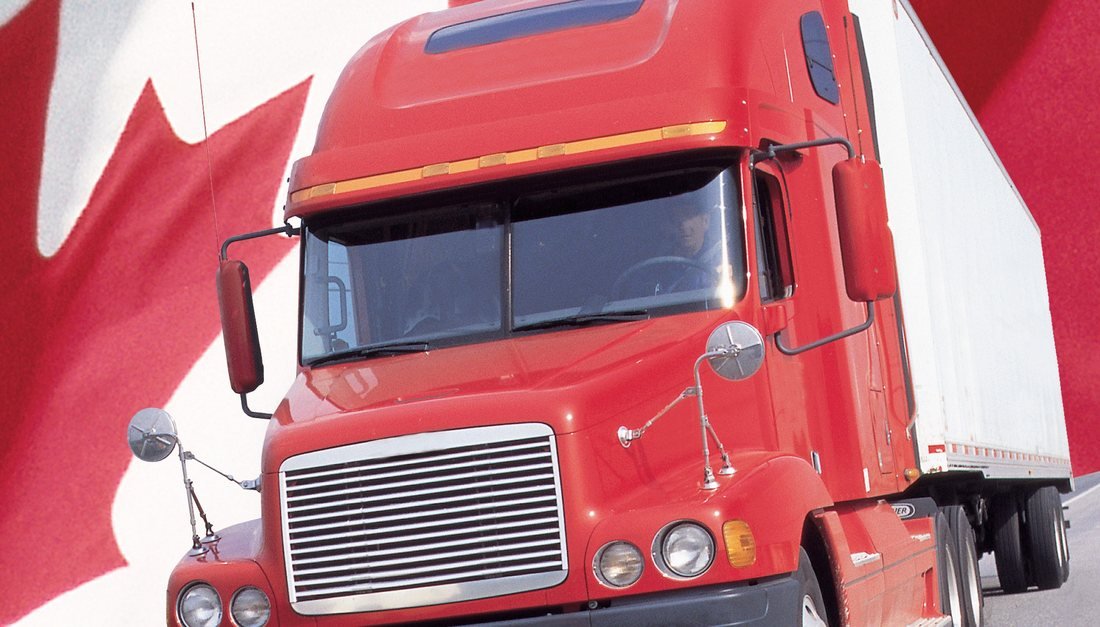 Camion Freightliner diesel rouge devant le drapeau canadien — le vrai coût d'une vidange diesel se mesure au kilomètre